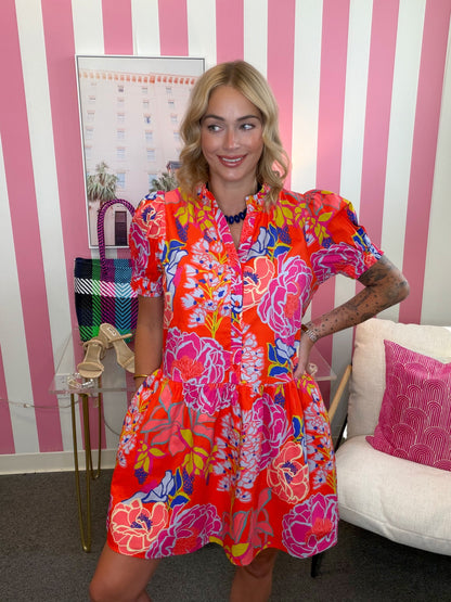 Woman in a colorful dress standing in a room with pink and white striped walls.
