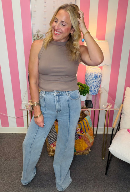 Woman in a brown top and light blue jeans standing in a room with pink and white striped walls.