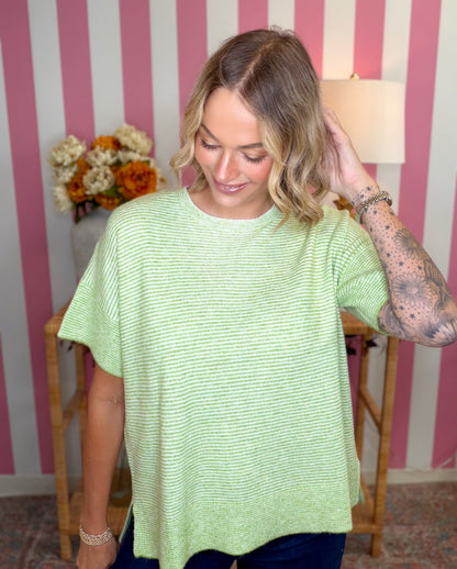 A woman wearing a light green and white striped short-sleeve t-shirt, standing in front of a pink and white striped wall.