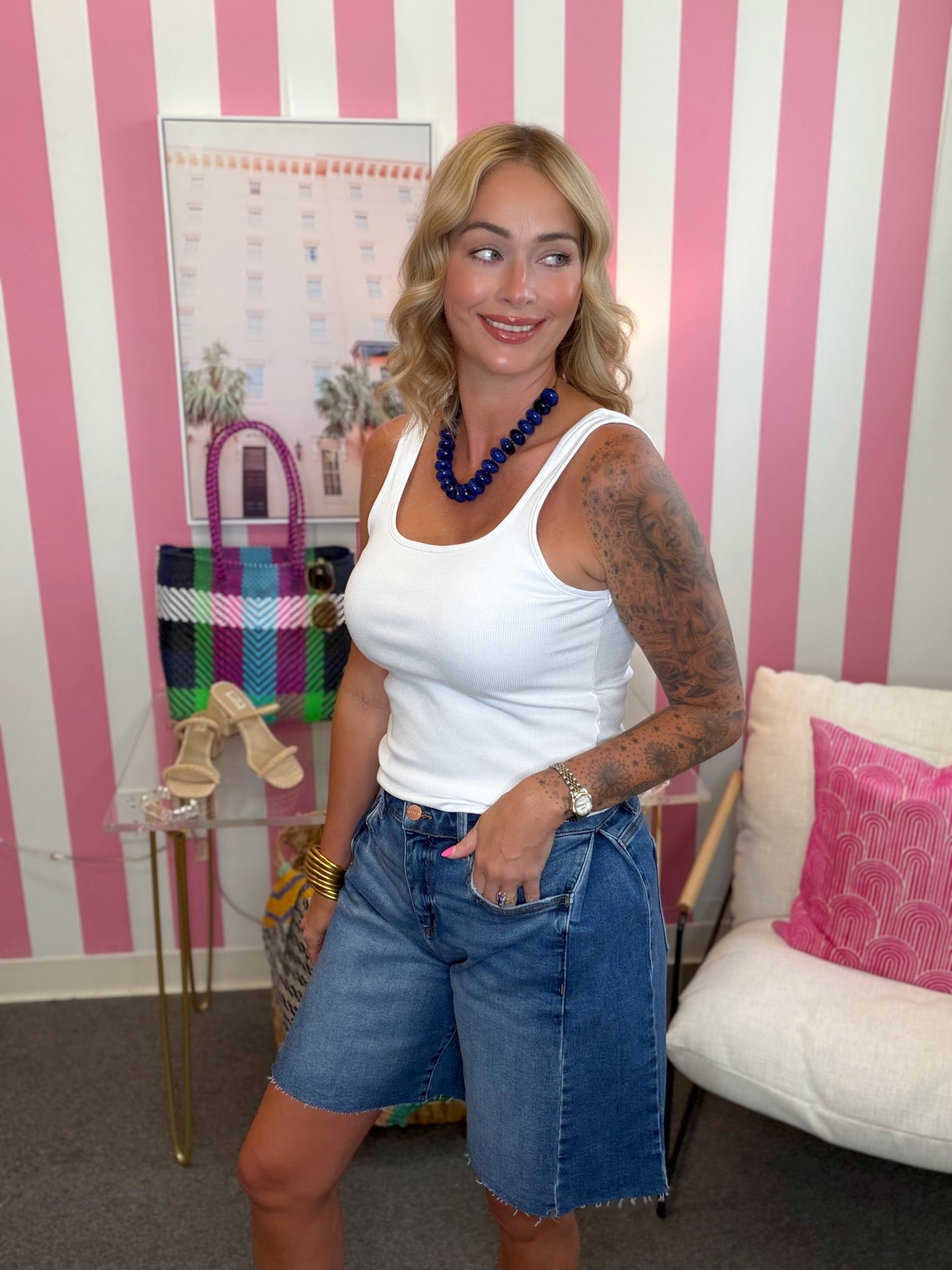 Woman in a white tank top and denim shorts standing in a room with pink and white striped walls.