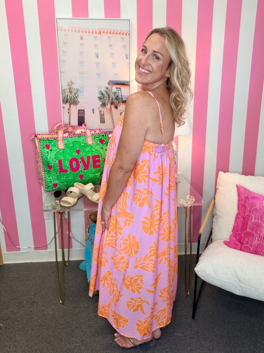 Woman in a pink floral dress standing in a room with striped walls and a colorful bag.