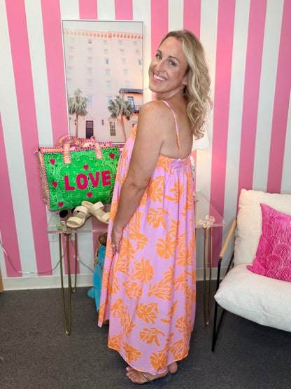 Woman in a pink floral dress standing in a room with striped walls and a colorful bag.