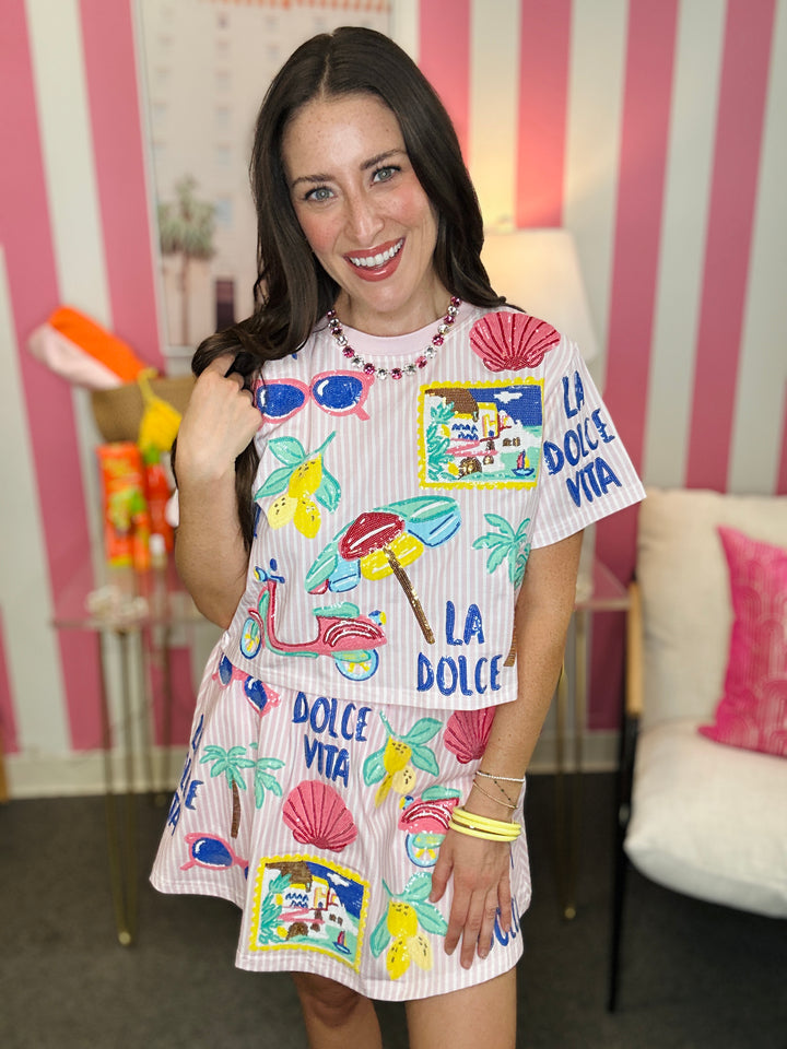 Woman wearing a colorful dress with various designs and text in a room with striped walls.