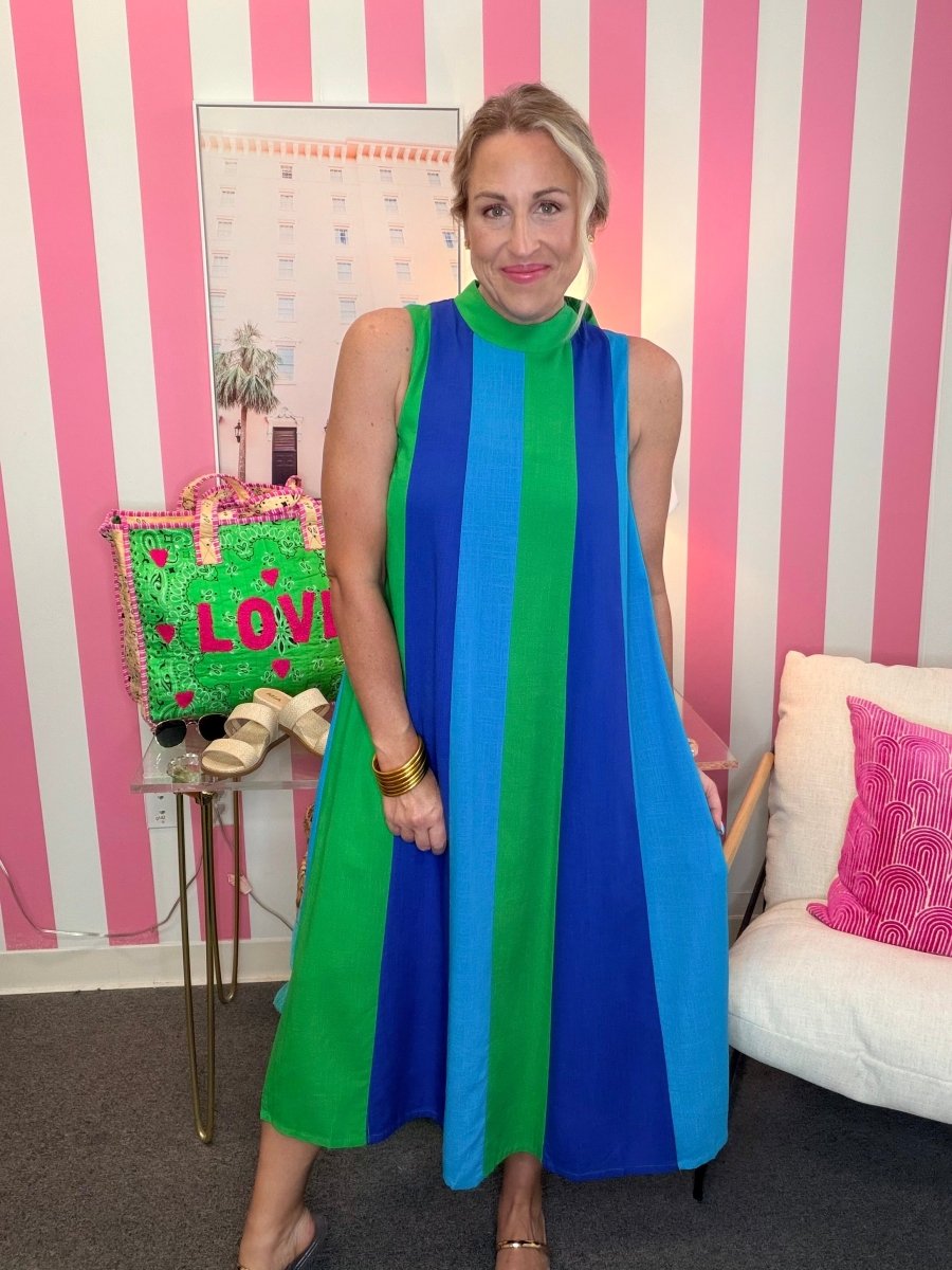 Woman in a colorful striped dress standing in front of a pink and white striped wall.