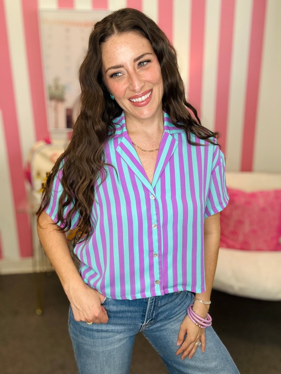 Woman wearing a purple and white striped shirt with jeans in a room with pink and white striped walls.