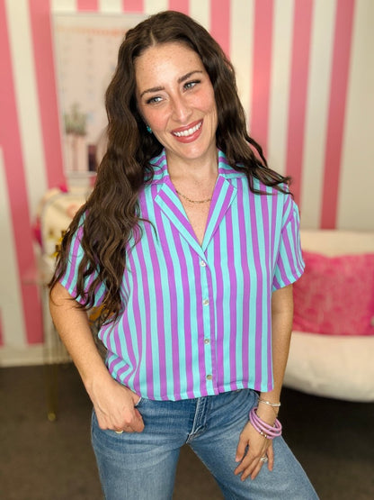 Woman wearing a purple and white striped shirt with jeans in a room with pink and white striped walls.