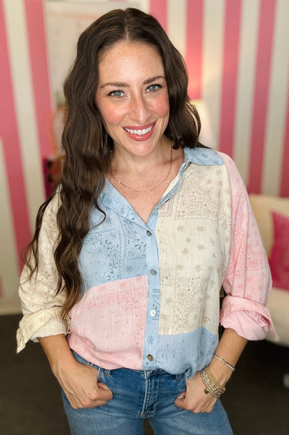 Woman wearing a patterned shirt with rolled-up sleeves in front of a striped wall.
