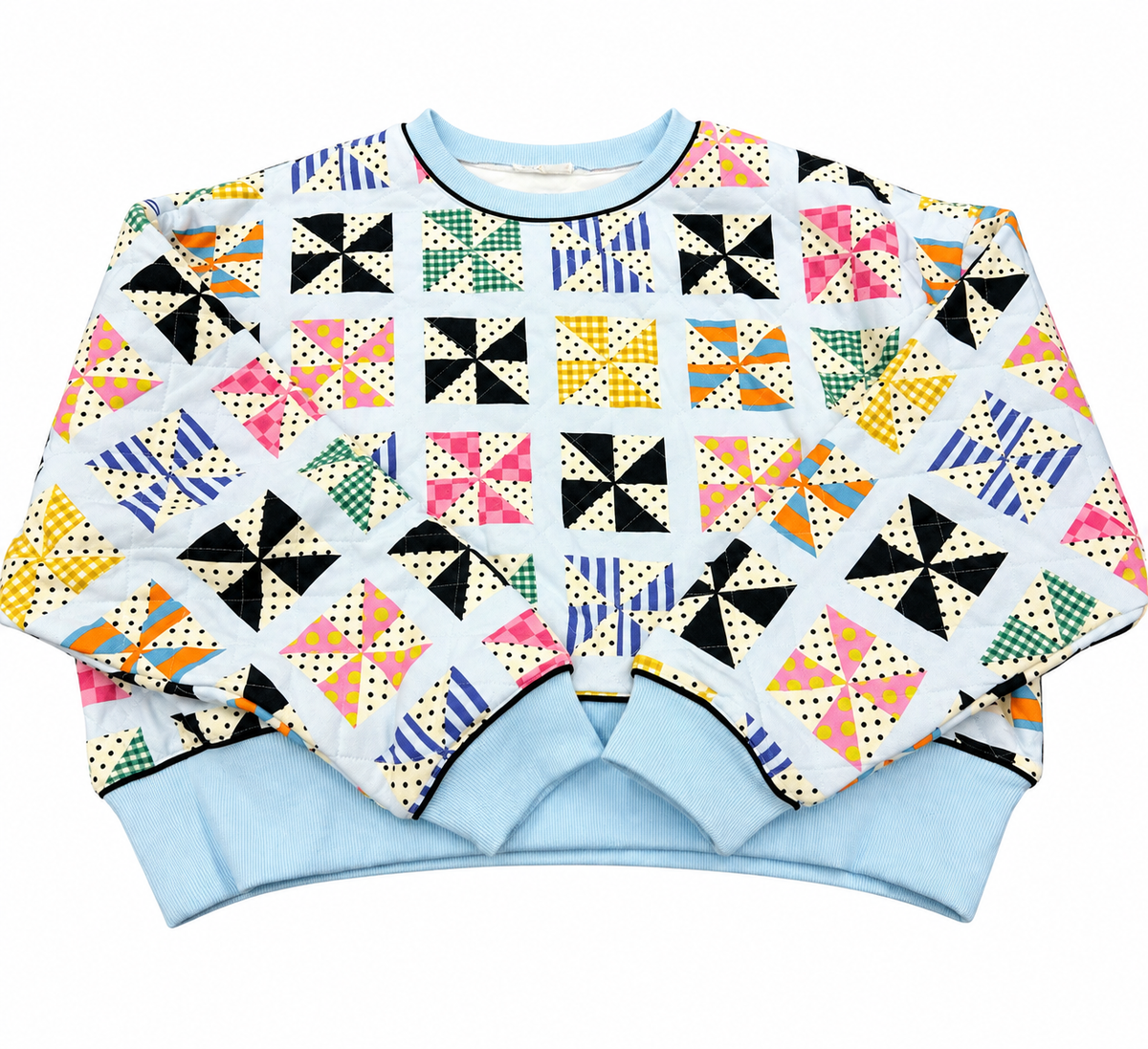 A long-sleeve crewneck sweatshirt featuring a colorful retro patchwork quilt pattern on a white background, with light blue ribbed cuffs and hem.