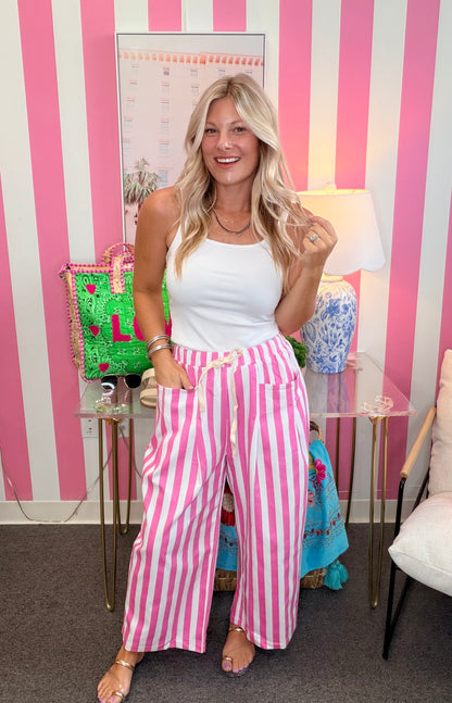 Woman in white top and pink striped pants standing in a room with a striped wall.