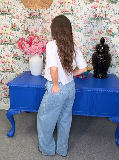 Person standing in front of a blue table with decorative items against a floral wallpapered wall.