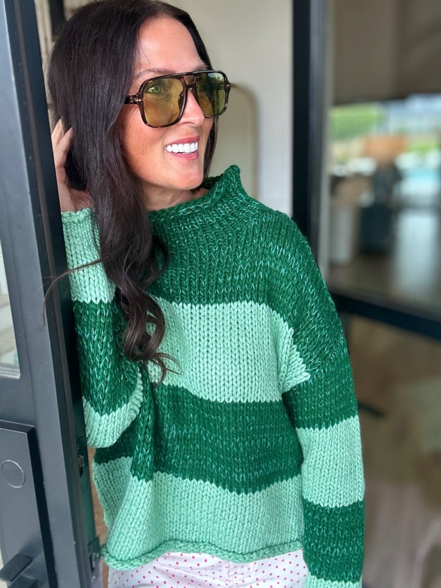 A smiling woman with black hair wearing a chunky knit sweater with green and mint green geometric blocks.