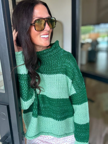 A smiling woman with black hair wearing a chunky knit sweater with green and mint green geometric blocks.