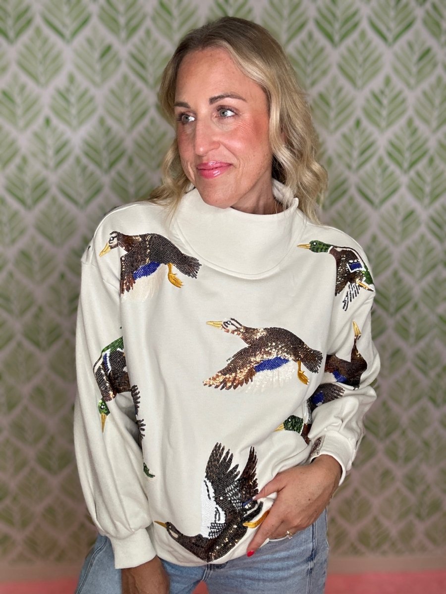 woman standing in a mock neck pullover with sequin ducks on it