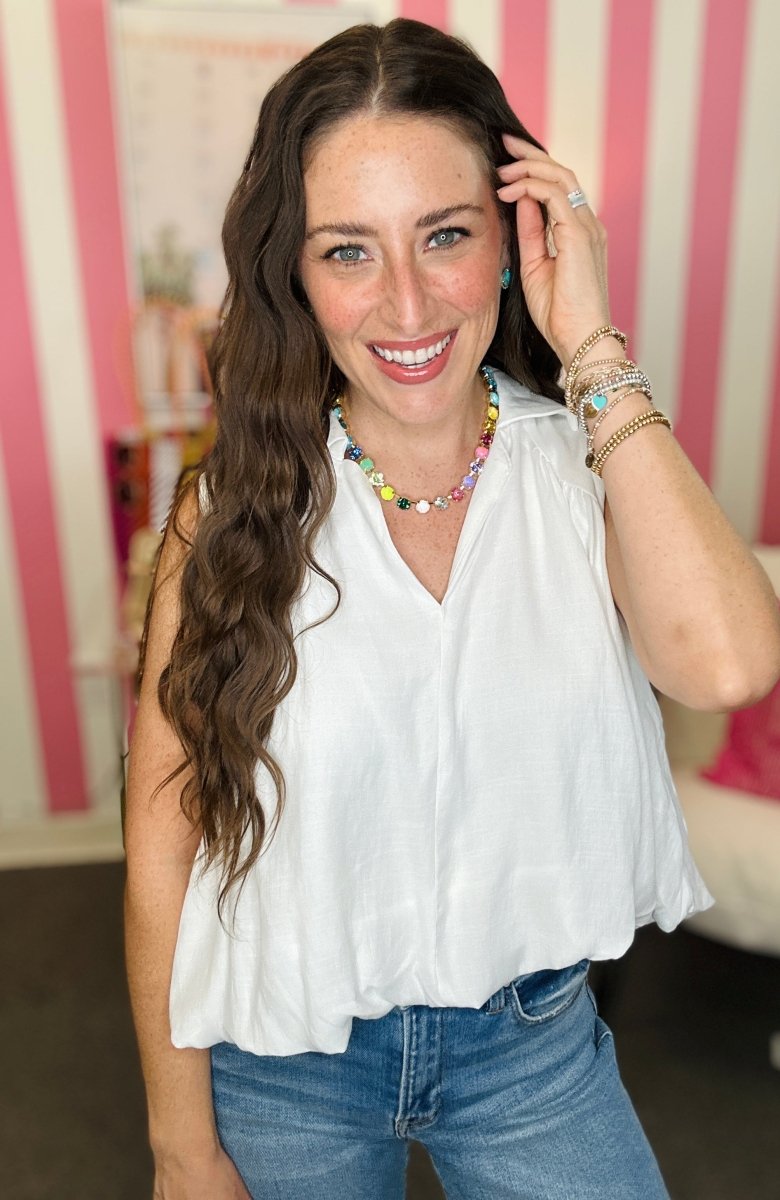Woman wearing a white sleeveless top and blue jeans with a colorful necklace and bracelets.