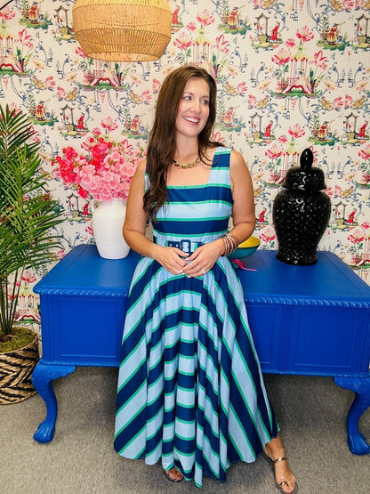 Woman in a striped dress sitting on a blue bench against a floral wall.