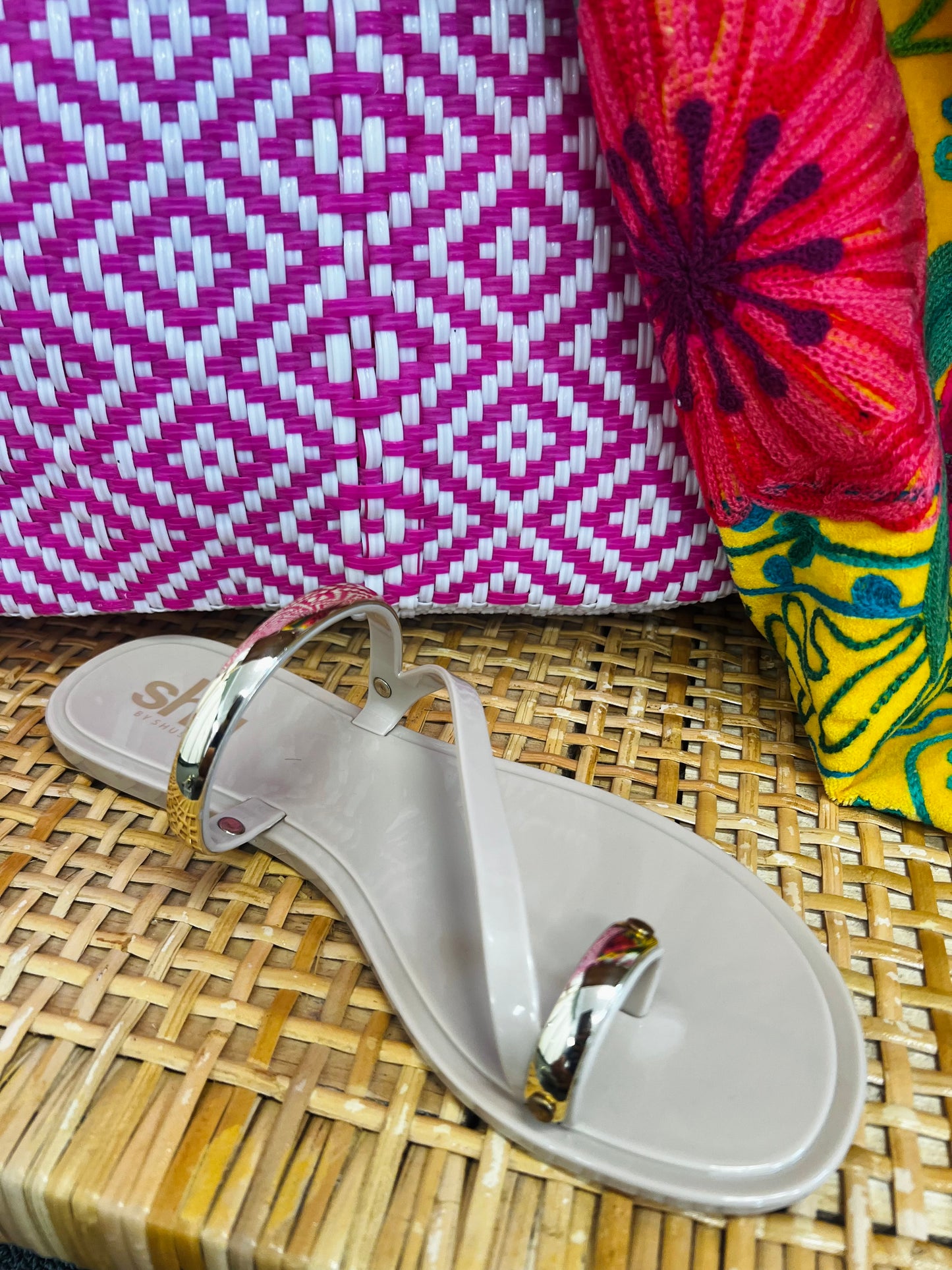 White sandal with gold accents on a woven surface, with colorful fabric in the background