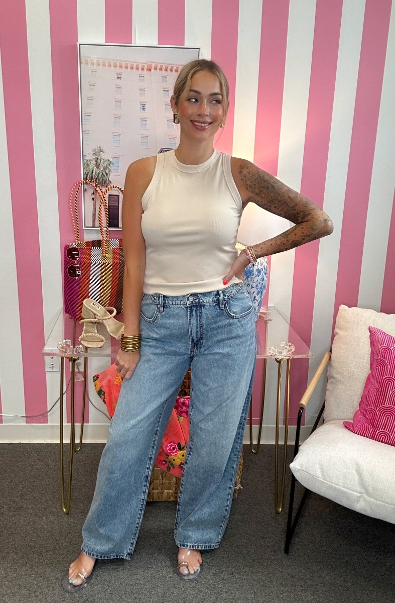 Woman in a white sleeveless top and blue jeans standing in a room with pink and white striped walls.
