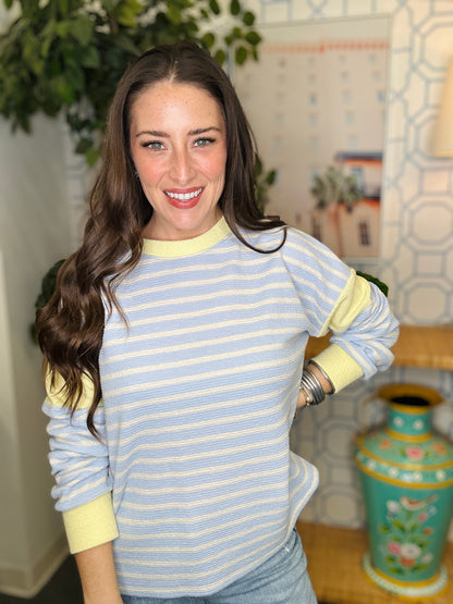 Woman wearing a blue and yellow striped sweater in a room with decorative elements.
