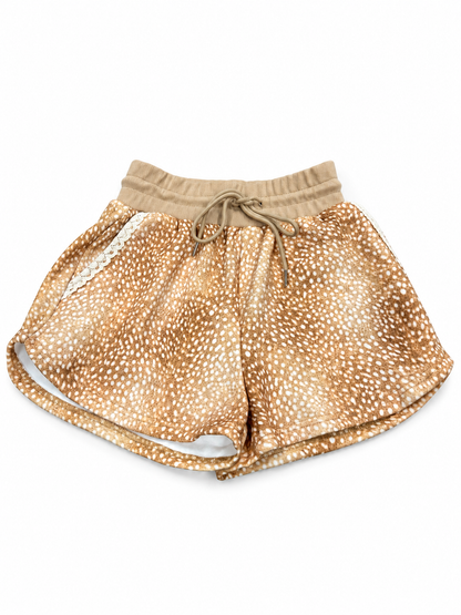A pair of women's shorts featuring a tan and white deer print pattern, with a solid tan elastic waistband and matching drawstring.