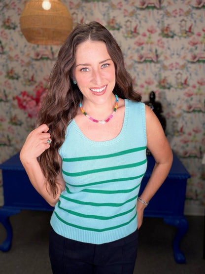 Woman wearing a light blue tank top with green stripes in a room with floral wallpaper.