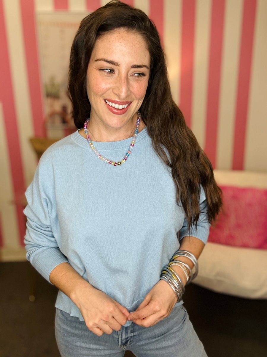 Woman wearing a light blue sweater and jeans with a striped wall in the background