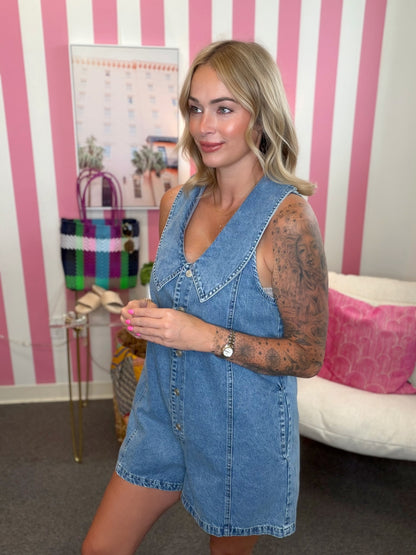 Woman wearing a denim romper in a room with pink and white striped walls.