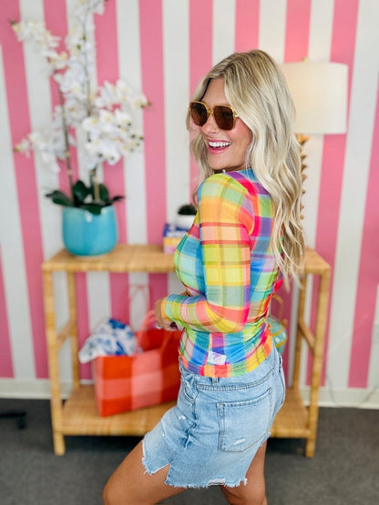 Woman wearing a colorful plaid shirt and denim shorts in a room with pink and white striped walls.