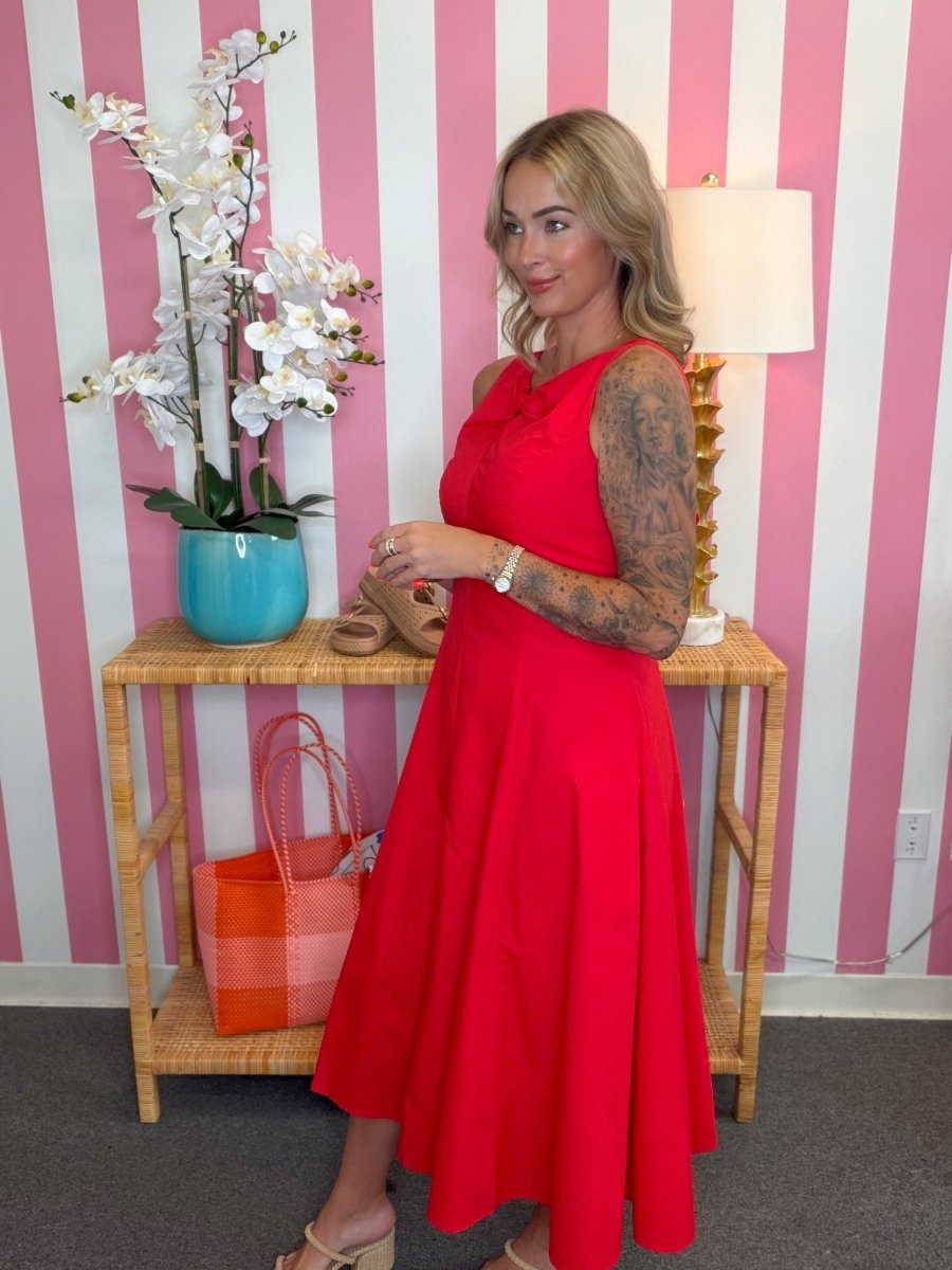 Woman in a red dress standing in front of a striped wall with a table and lamp.