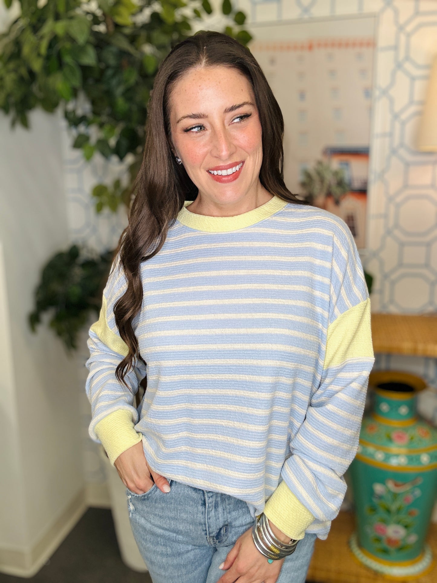 Woman wearing a striped sweater with a decorative vase and plant in the background