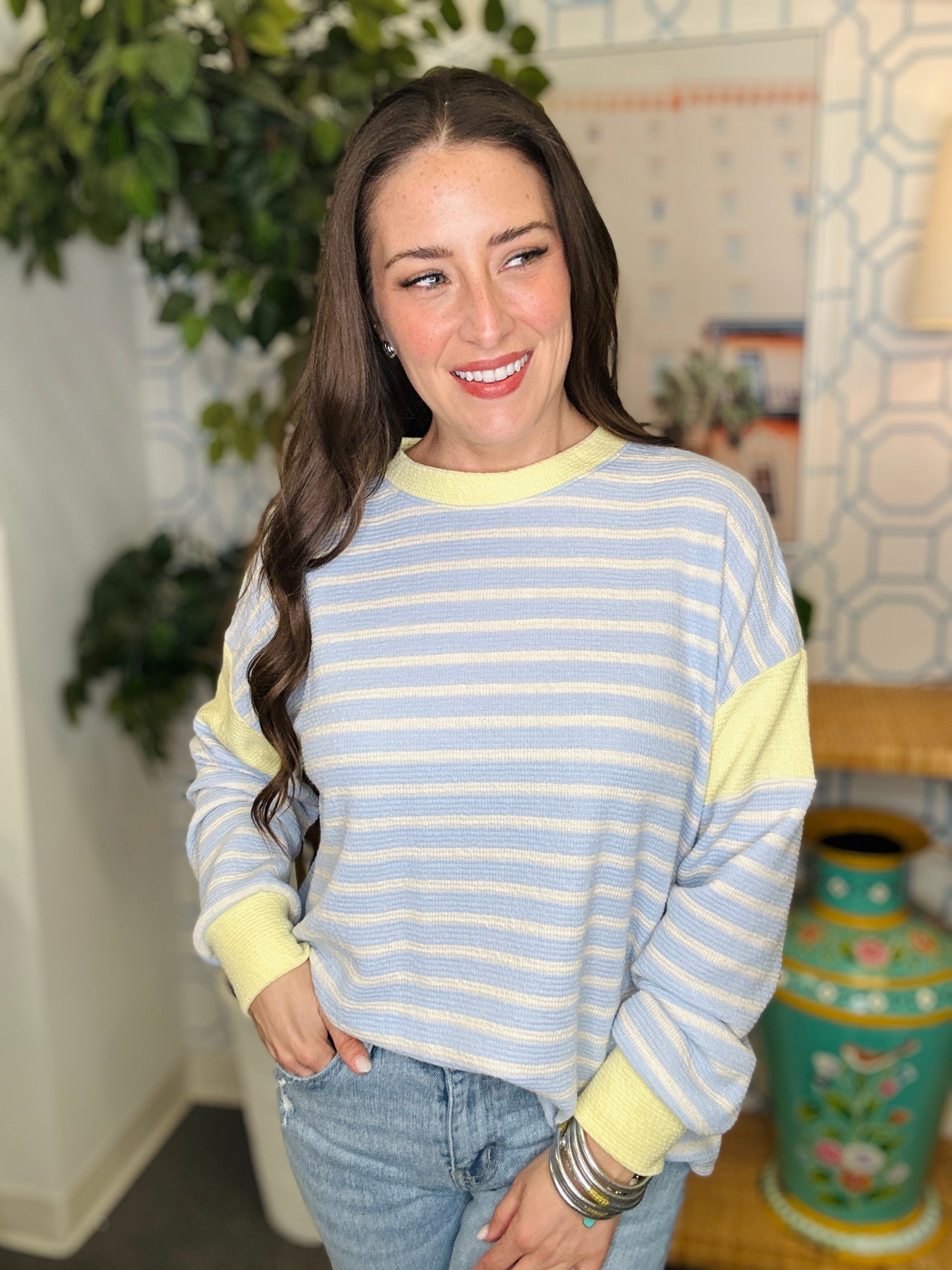 Woman wearing a striped sweater with a decorative vase and plant in the background