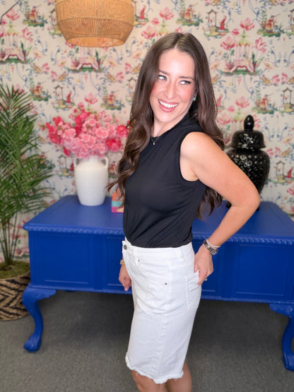 Woman in black sleeveless top and white shorts standing in a room with floral wallpaper and a blue table.