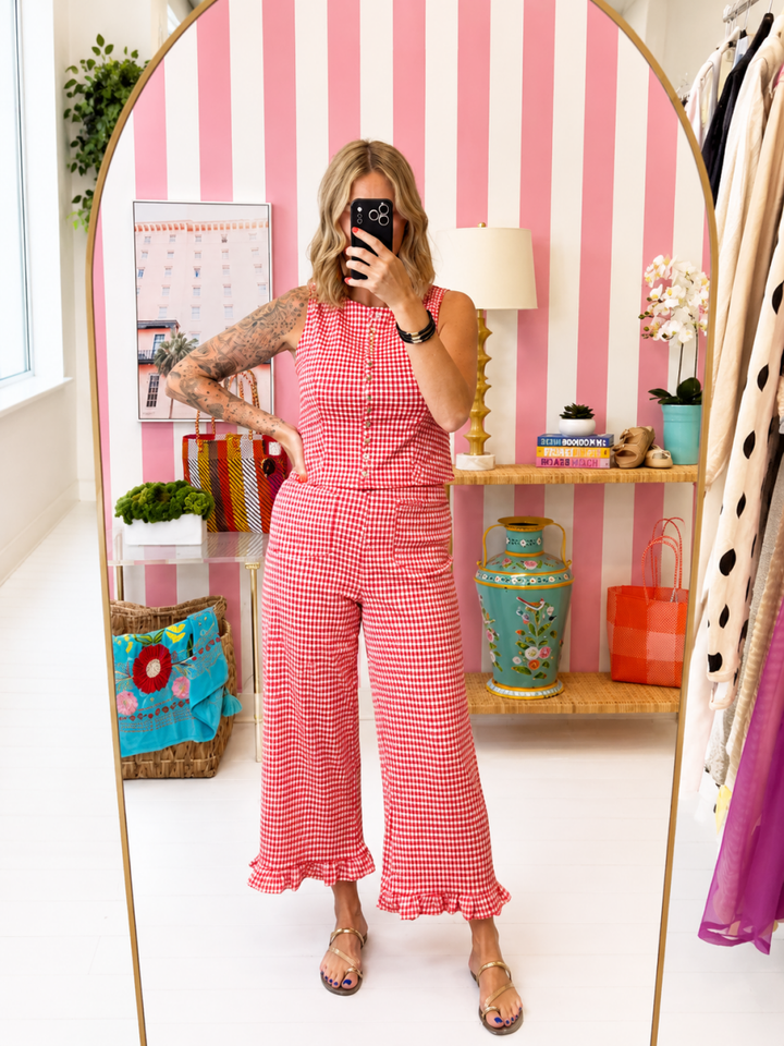 Woman taking a mirror selfie wearing a red checkered outfit in a room with a striped pink and white wall.