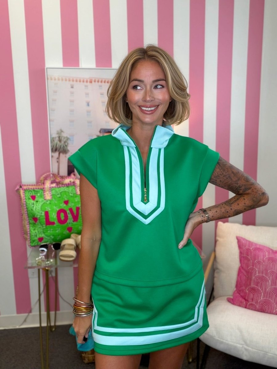 Woman wearing a green dress with white trim in a room with pink and white striped walls.