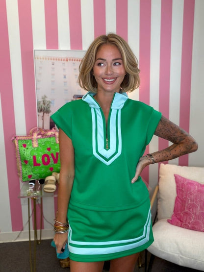 Woman wearing a green dress with white trim in a room with pink and white striped walls.