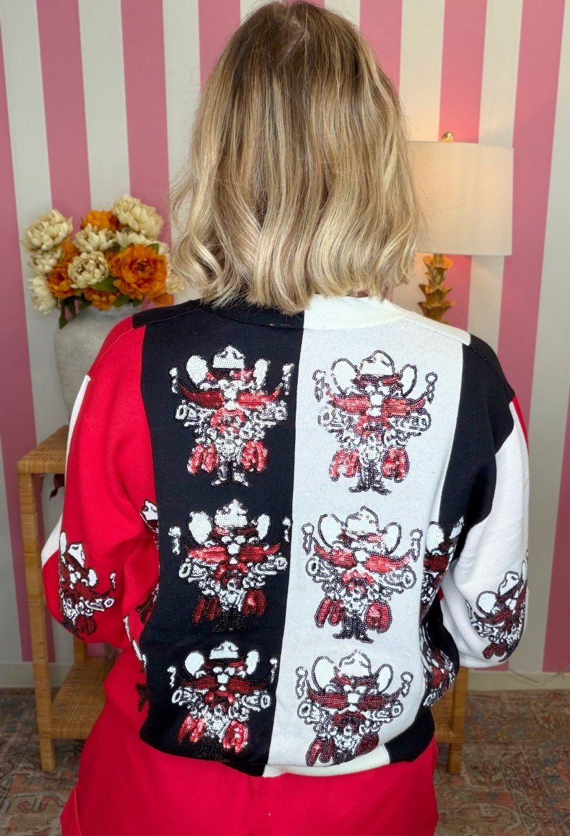 A person viewed from behind wearing a long-sleeve color-block jacket with a black and white center panel, each printed with a red, white, and black cartoon cowboy character. The jacket also has solid red sleeves and side panels.