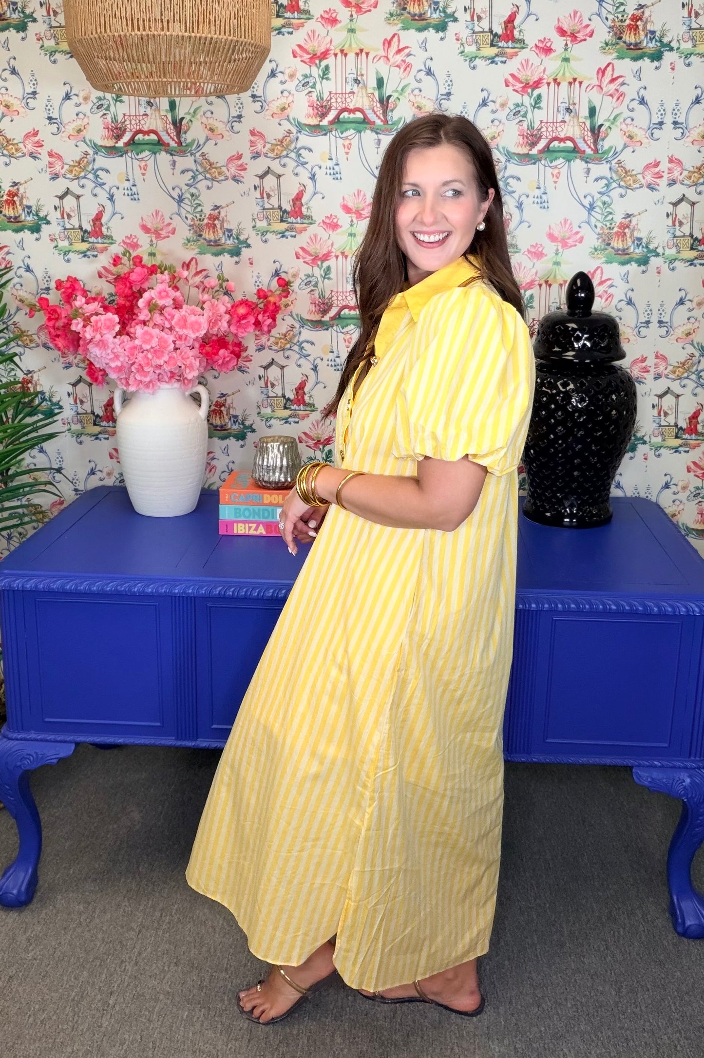Woman in a yellow dress standing in front of a colorful wall with floral patterns.