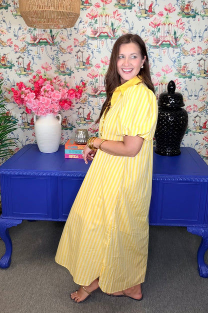 Woman in a yellow dress standing in front of a colorful wall with floral patterns.