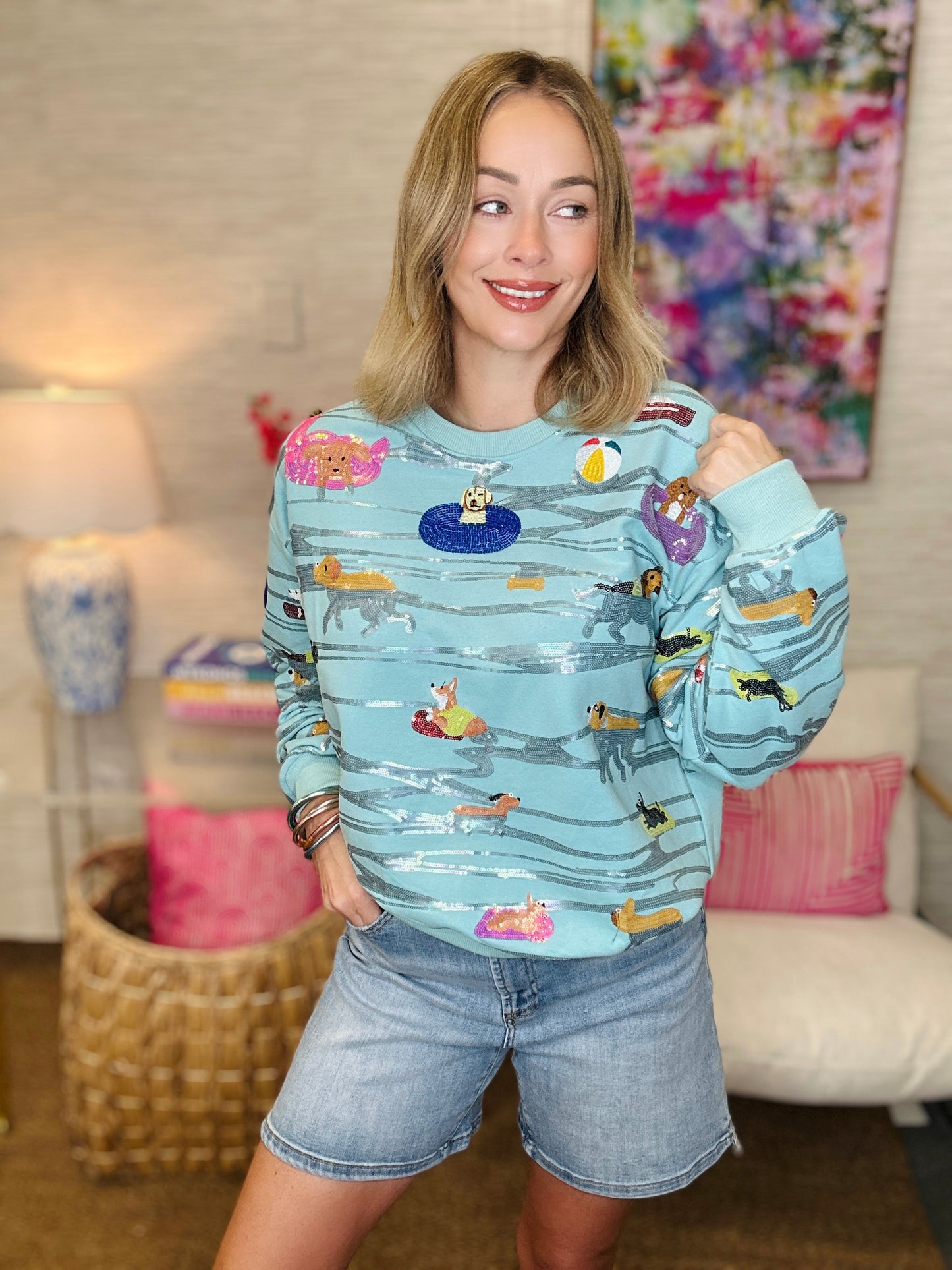 Woman wearing a light blue sweatshirt with dog patterns in a living room.