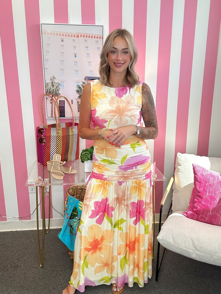 Woman in a colorful floral dress standing in a room with striped walls and furniture.