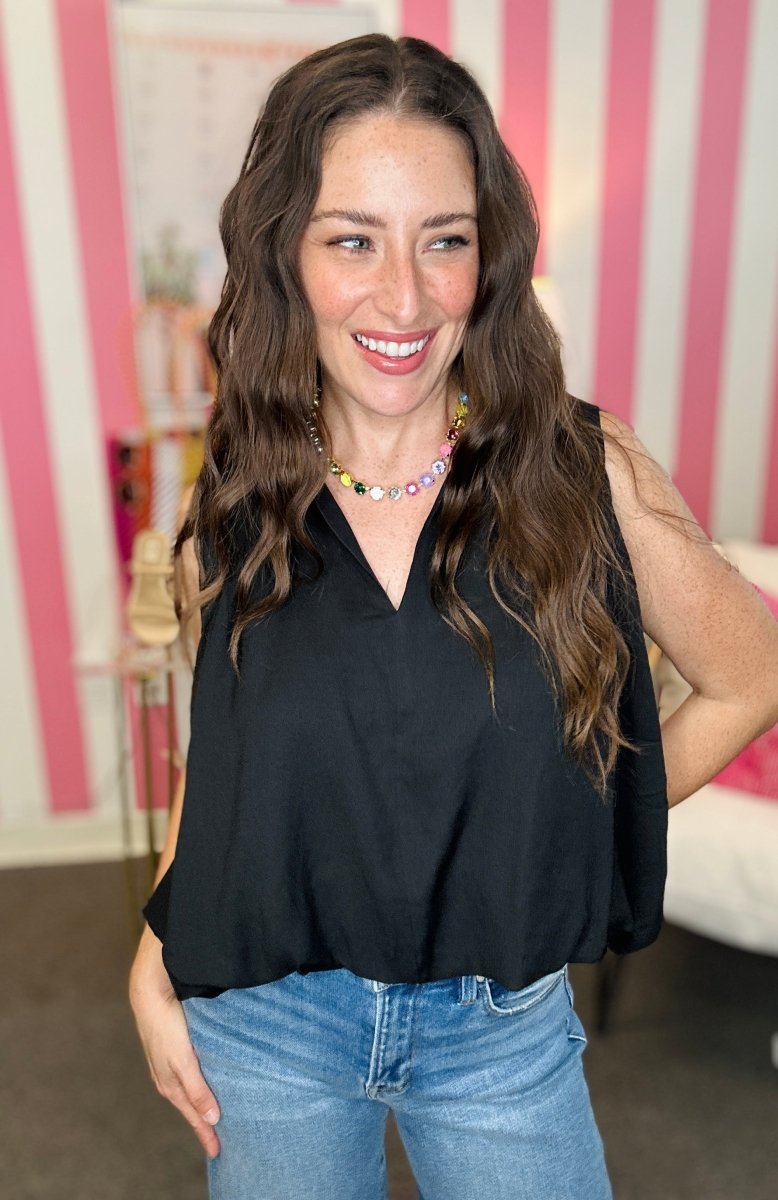 Woman wearing a black top and blue jeans indoors with pink and white striped wall.