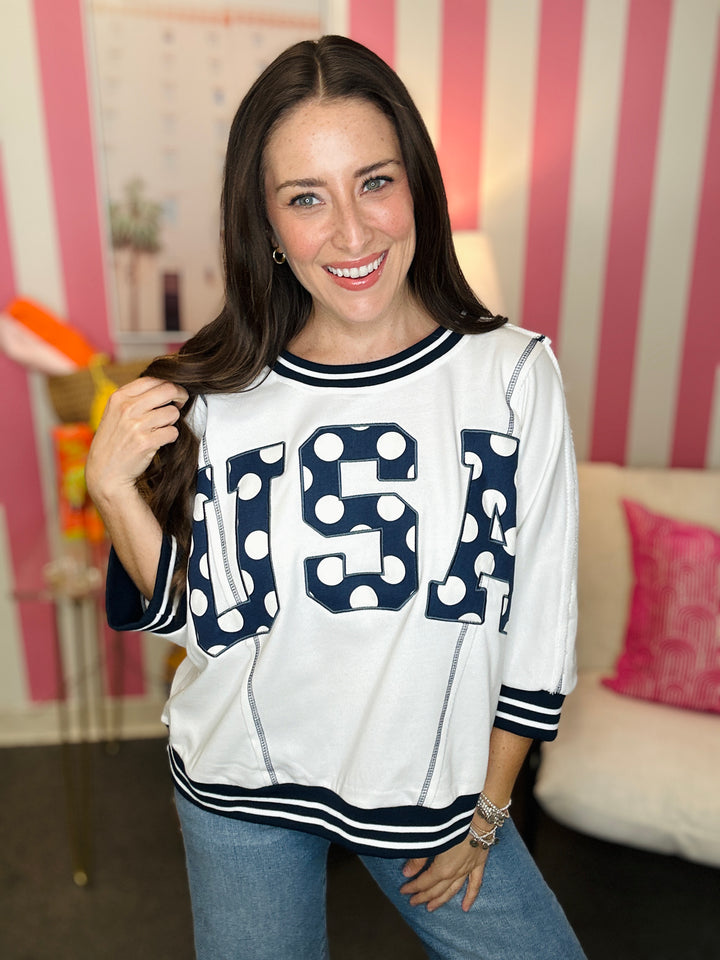 Woman wearing a white sweatshirt with 'USA' printed on it in a casual setting.