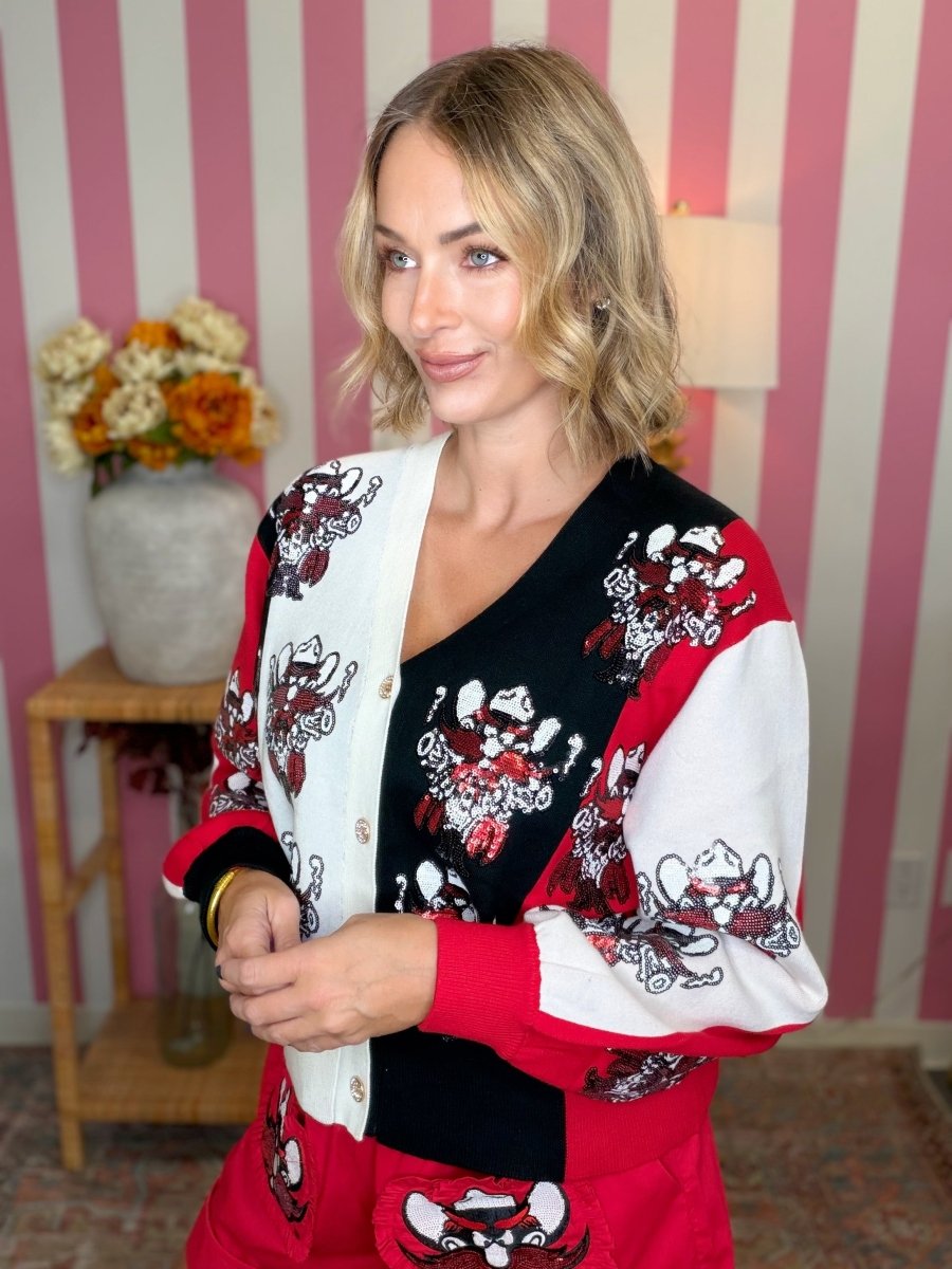A woman wearing a red, black, and white cartoon-patterned cardigan and matching red bottoms, standing in front of pink and white striped wallpaper.