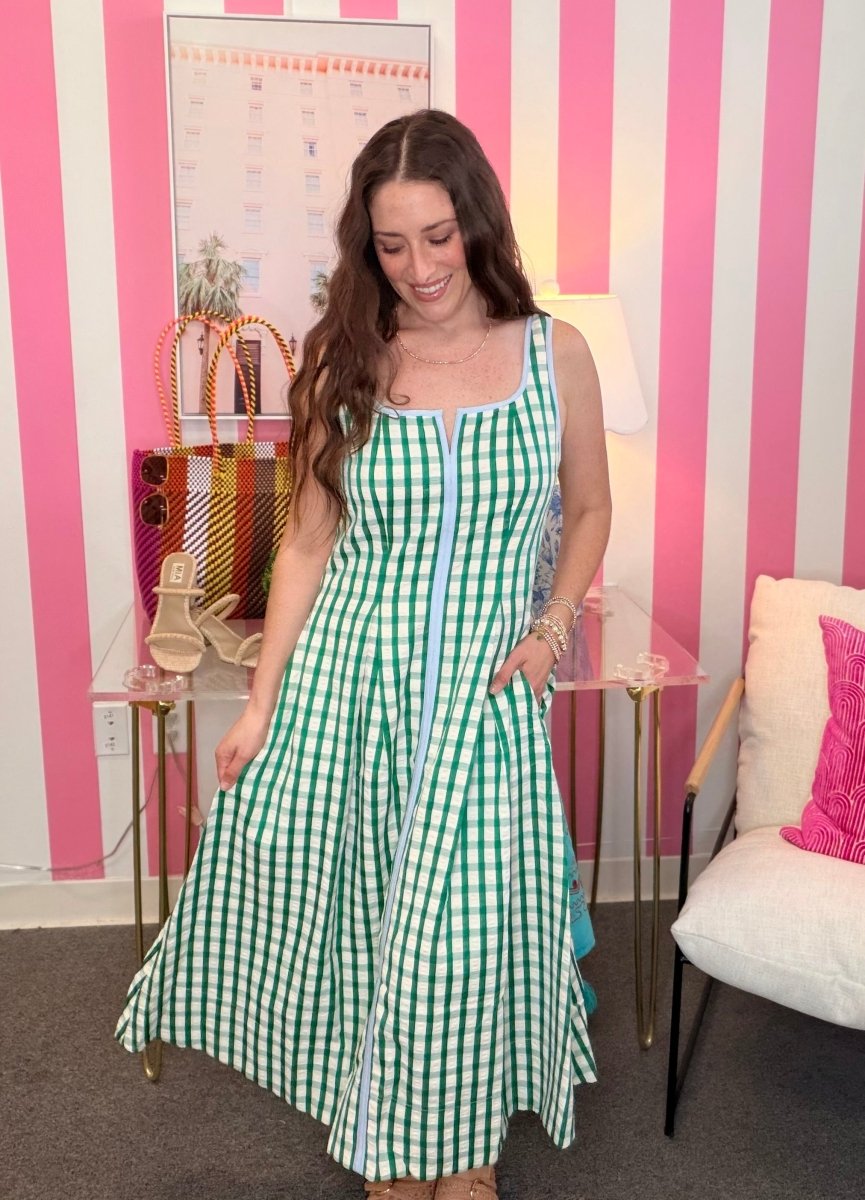Woman in a green and white checkered dress standing in a room with pink and white striped walls.