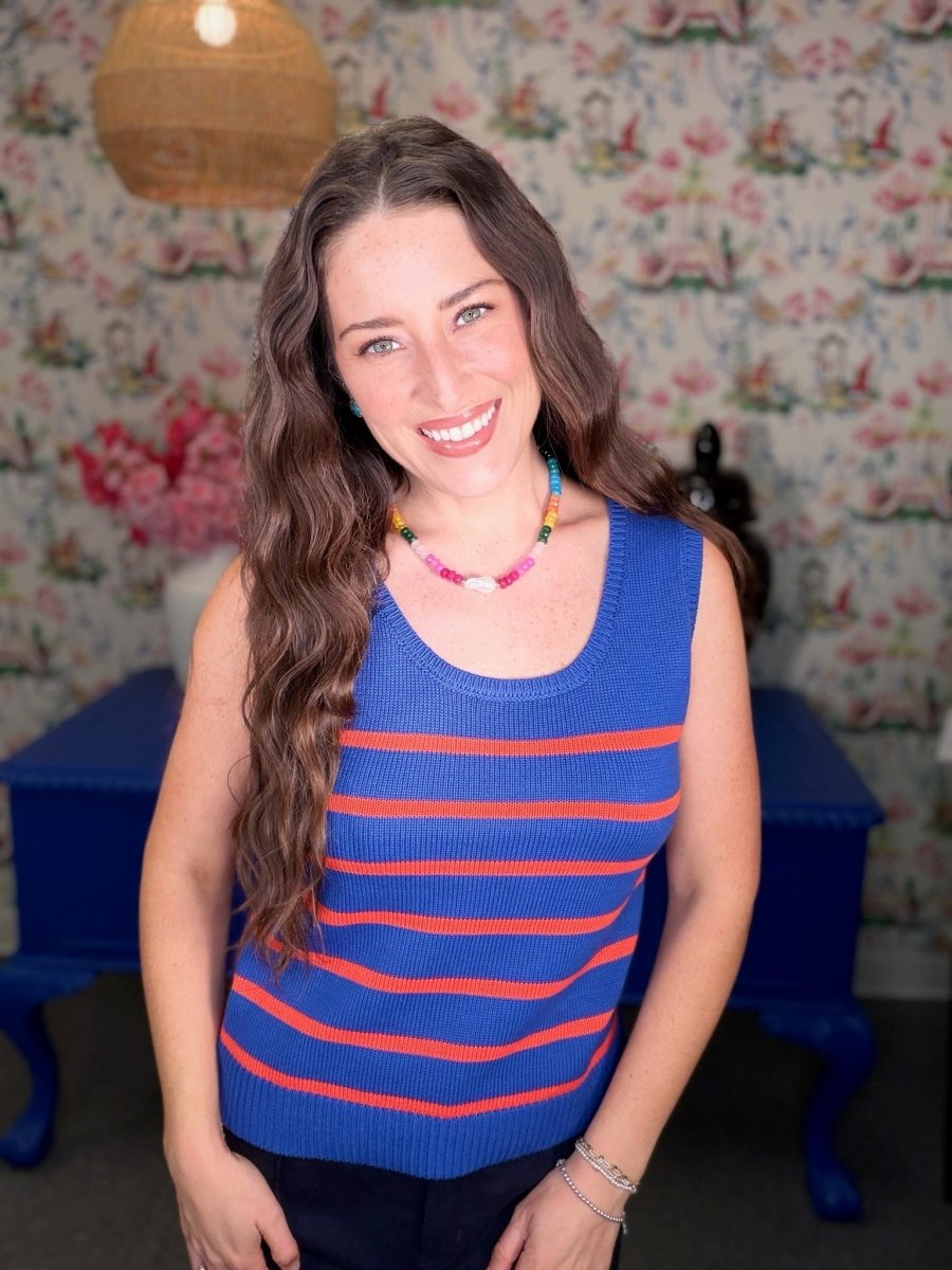 Woman wearing a blue and red striped sleeveless top in a room with floral wallpaper.