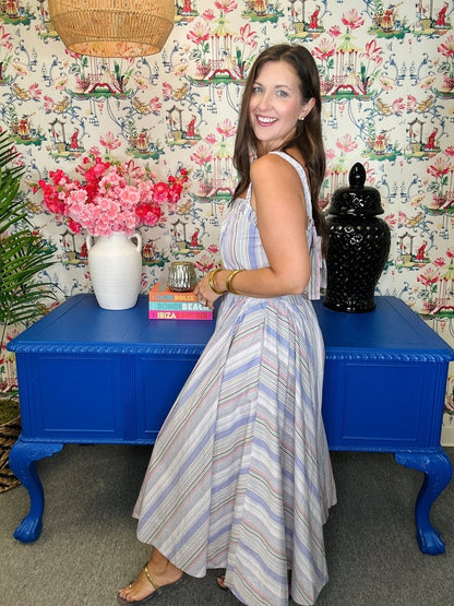 Woman in a striped dress standing next to a blue table with decorative items against a patterned wall.