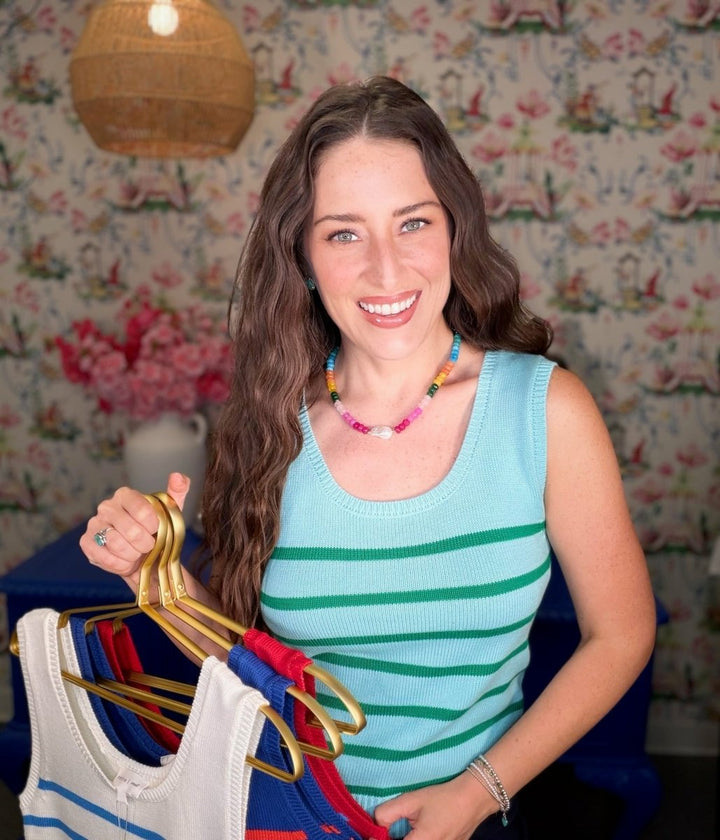 Woman holding a rack of clothes against a colorful floral wallpaper background