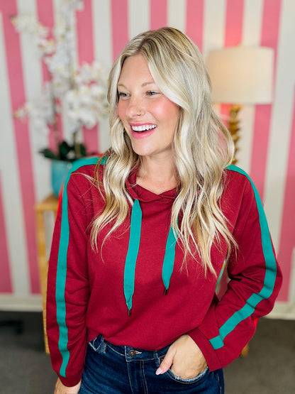 Woman wearing a red hoodie with green accents in a room with pink and white striped walls.
