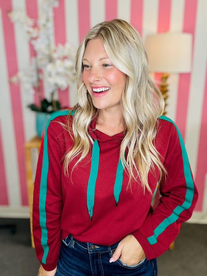 Woman wearing a red hoodie with green accents in a room with pink and white striped walls.