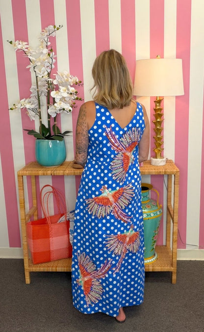 Woman wearing a blue polka dot dress with bird patterns in a room with striped walls.