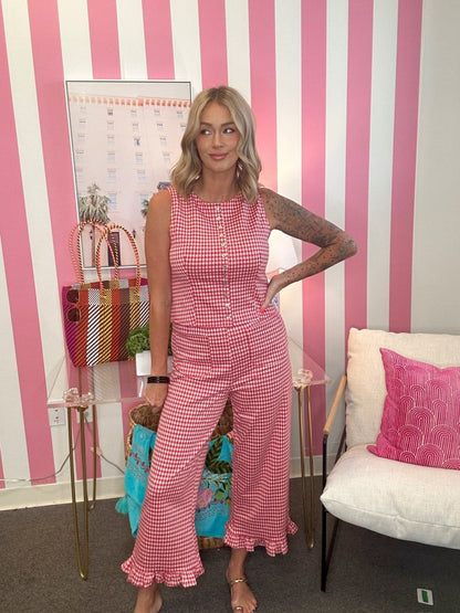 Woman in a pink checkered jumpsuit standing in a room with striped walls and a white couch.